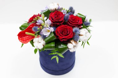 Parlak bir buket kırmızı çiçek (gül ve anthurium) yeşil yaprakları, mavi bir kutu için hafif bir arka plan üzerinde şapka Alstroemeria ve pamuk çiçeklenir