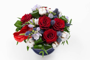 Parlak bir buket kırmızı çiçek (gül ve anthurium) yeşil yaprakları, mavi bir kutu için hafif bir arka plan üzerinde şapka Alstroemeria ve pamuk çiçeklenir