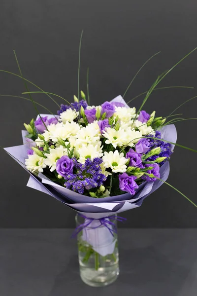 Bright bouquet of bright colors in paper packaging against a gray background.