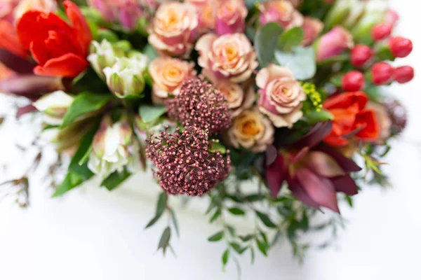 Flower arrangement of bright fresh flowers of different varieties (colors: red, pink, white, green) in a white cardboard box on a bright background