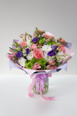 Etkileyici buket taze çiçek (ana renkler: beyaz, pembe, yeşil, mor) hafif bir arka plan üzerinde bir vazoda bir kağıt pakette.