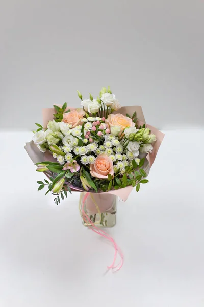 Delicate bouquet of fresh flowers (Main colors: white and pink) in a paper packaging in a vase on a light background.