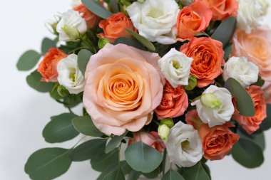 Gül (beyaz, pembe, turuncu) narin çiçek düzenleme ve yeşil okaliptüs yaprakları bir yuvarlak beyaz karton kutunun içinde hafif bir arka plan üzerinde