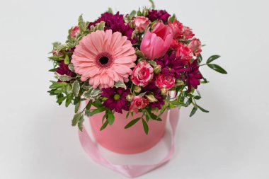 Taze çiçekler (Gül, Gerbera, Lale) (renkler: sakal, pembe, yeşil, beyaz) hafif bir arka plan üzerinde pembe karton yuvarlak şapka kutusu etkileyici bir eşleştirme kompozisyon