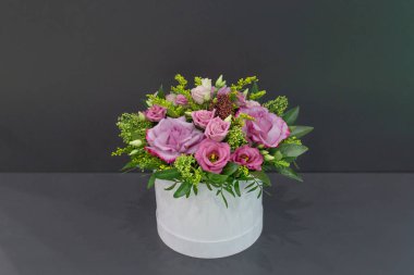 Gri bir arka plan üzerinde bir şapka kutusunda yaprakları ile gül ve egzotik çiçekler etkileyici bir kompozisyon