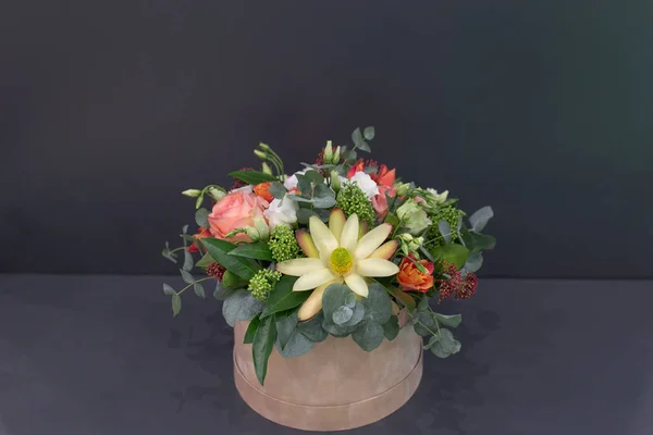 An impressive composition of roses and exotic flowers with leaves in a hat box on a gray background