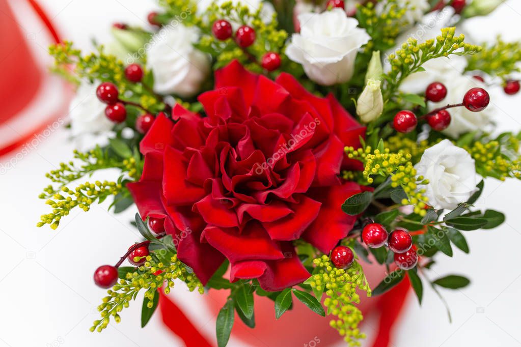 Life-affirming composition of fresh flowers (Rose, Eustoma, Solidaga, Pistachio leaves) and decorative berries in a scarlet cardboard round hat box on a light background