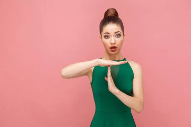 Kamera pembe bir arka plan, ifade duygu ve duyguları kavramı zaman aşımı işaret gösteren yeşil giysili toplanan saçlı güzel kadın 