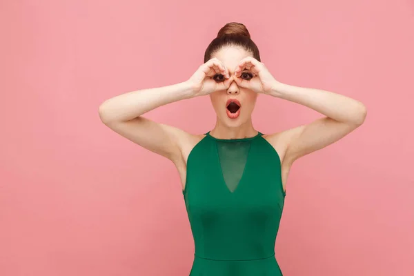 woman with bad sight showing binoculars sign on pink background. Expression emotion and feelings concept