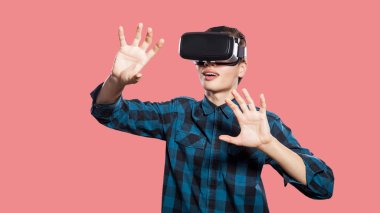 mutlu gülümseyen genç adam pembe bir arka plan üzerinde hayali gerçeğe dokunmak baş trying üzerinde vr kulaklık ile damalı gömlek giymiş