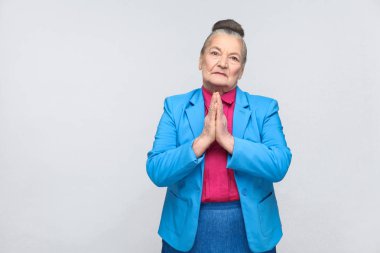 Mavi takım ve pembe gömlek elinde tutan etkileyici Büyükanne özür jest gri arka plan üzerinde