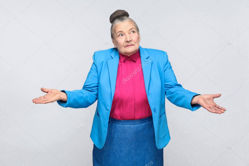 confused old woman in blue suit and pink shirt with divorced hands posing on gray background, Expression emotion and feelings concept   