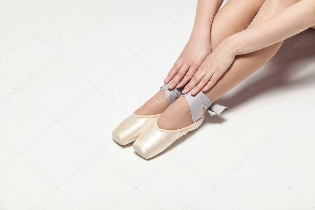 ballerina in pointe shoes sitting on white floor, close-up 