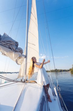 Beyaz yazlık elbise arka planda gökyüzü ile yatta poz süre ipleri tutan güzel kadın