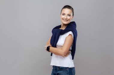 Çapraz elle gülümseyen ve gri arka plan üzerinde kameraya bakarak dişlek rahat kıyafet kadında