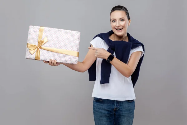 Beautiful wondered woman in blue jeans and sweater on shoulders and smart watch pointing at gift box, Expression and feelings concept