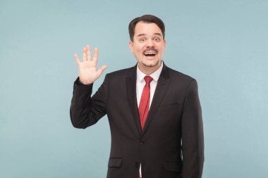 Pozitif patron siyah takım ve Merhaba işaret gösteren ve açık mavi renkli kameraya gülümseyen kırmızı kravat  