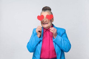 gözler önüne iki kırmızı küçük kalp işareti gri arka plan üzerinde tutan mutlu yaşlı kadın