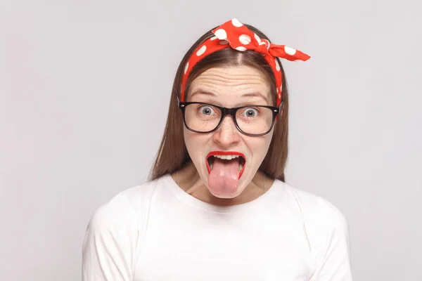 Stock image young woman with tongue out in white t-shirt and glasses on light gray background