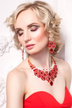 Kıvırcık saç ve güzel makyaj şık mücevher beyaz duvar arka plan kapalı gözler ile poz giyen genç sarışın model 