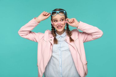 Hippi tarzı iki mavi ve pembe gözlük tutan ve uzak dişlek gülümseme ile yeşil arka plan üzerinde seyir helezon saç modeli ile mutlu komik kadın