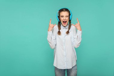 çizgili mavi gömlekli kulaklık favori müzik dinleme ve rock işareti yeşil arka plan üzerinde gösterilen süre ile sürpriz yüz kameraya bakarak mutlu hayran kadın
