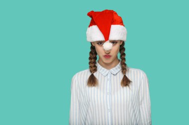 çizgili mavi gömlek ve kırmızı Noel kap ayakta ve yeşil arka planda, yeni yıl kavramı kameraya bakarak helezon kıllar ile komik güzel kadın 