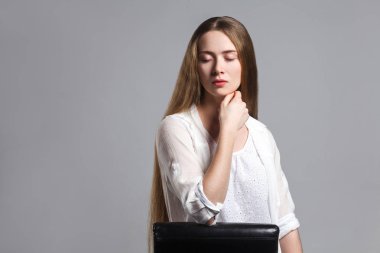 Deniz tarağı portresi siyah sandalyede oturan ve çenesi ile dokunmadan beyaz t-shirt uzun kahverengi saçlı güzel genç model oyuncu kapalı gözler gri arka plan üzerinde