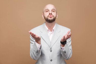 mutlu yakışıklı orta yaşlı kel işadamı ışık gri elbiseli kameraya bakarak ve kahverengi arka plan üzerinde hava öpücük gönderme sakallı