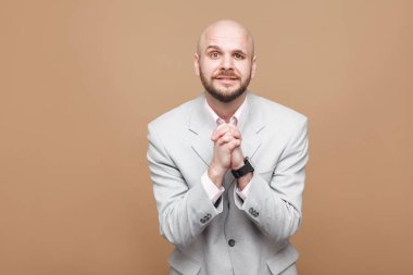  Orta yaşlı kel sakallı işadamı işçisi ışık gri elbiseli ayakta ve kameraya umutlu yüzü kahverengi zemin üzerine arıyorum.