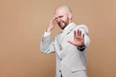 Orta yaşlı kel portresi el ile işadamı kapalı burun ile ışık gri elbiseli sakallı ve gösteren kötü koku kahverengi zemin üzerine işaret