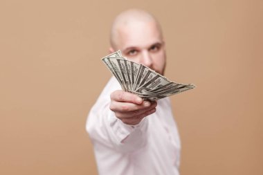 mutlu yakışıklı orta yaşlı kel işadamı tutarak ve kahverengi arka plan üzerinde kameraya bakarken dolar gösterilen beyaz gömlekli sakallı