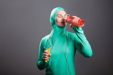 Turuncu gri arka plan kapalı gözler şişeyle içme yeşil İslam spor giyim kadında güzel rahat atlet