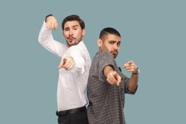 two handsome bearded friends looking and pointing at camera with funny amazed faces on blue background  clipart