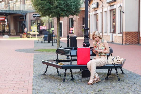Junge Frau Sitzt Nach Einkauf Auf Bank Und Benutzt Smartphone — Stockfoto