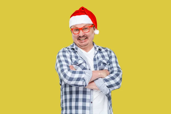 黄色の背景に交差した腕を持つ赤いサンタ帽子で幸せな中年の男 — ストック写真