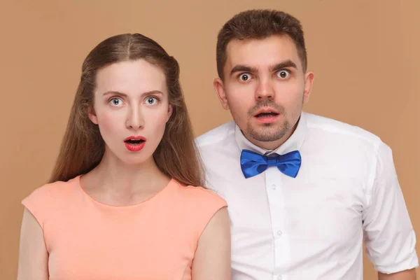 年轻夫妇的肖像看着惊奇惊讶的面孔和大眼睛在棕色背景的相机 — 图库照片