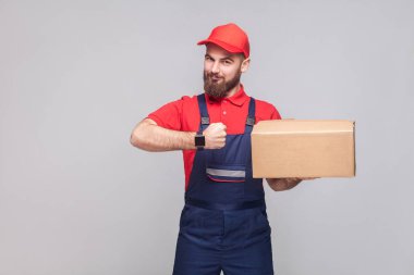 karton kutu tutarak ve gri arka plan, kavramı üzerinde saat teslimat hizmeti saati gösteren mavi üniforma ve kırmızı t-shirt genç lojistik sakallı adam 