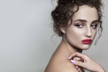Genç güzel manken toplanan siyah kıvırcık saçlı ve uzağa arıyorsunuz ile ciddi bir yüz gri arka plan üzerinde kırmızı dudaklar ile çıplak makyaj güzellik profil yan görünüm
