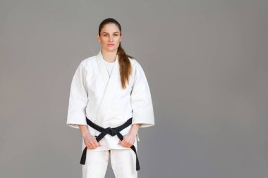 Ciddi yüz, Japon dövüş sanatları kavramı ile kameraya ararken holding siyah kuşak ve beyaz kimono duran güzel atletik genç kadın