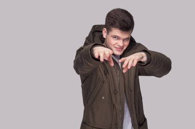 Işık gri gömlek ve koyu yeşil parka kameraya bakarak ve eller fotoğraf gri arka plan üzerinde gösterilen genç komik yakışıklı adam portresi