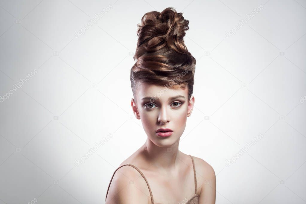 portrait of attractive brunette woman with stylish hairdo and makeup looking at camera on grey background 