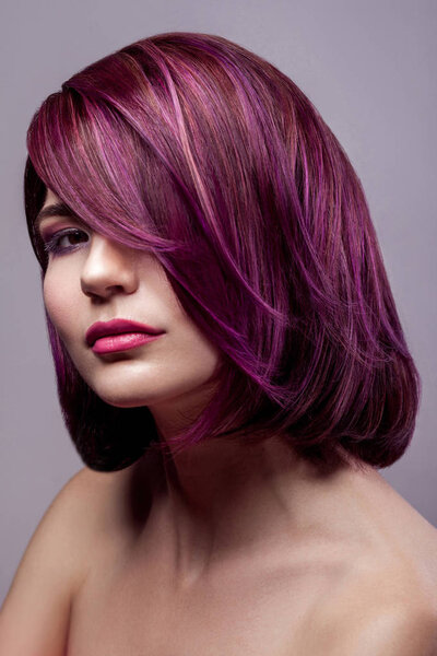 portrait of happy beautiful fashion model woman with short purple colored hairstyle and makeup looking at camera on gray background.