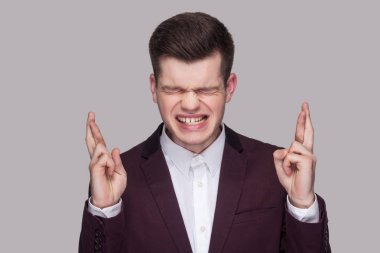 Menekşe takım elbise ve beyaz gömlek kapalı gözler holding ile umutlu rüya yakışıklı genç adam portresi gri arka plan üzerinde parmak çarpı işareti.