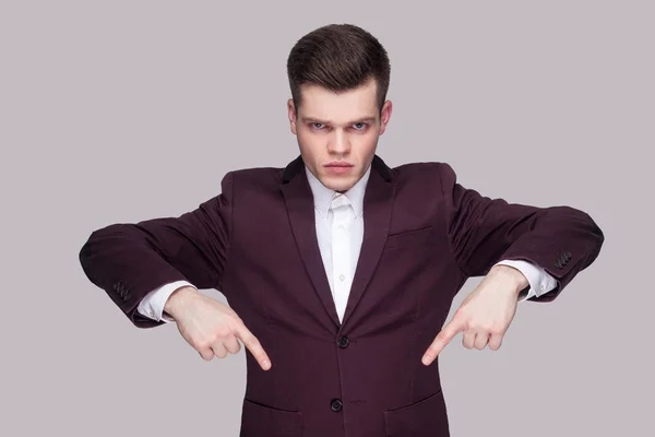 紫のスーツと白いシャツ カメラ目線と灰色の背景に上げられた腕を持つ下向き深刻なハンサムな若い男の肖像 — ストック写真