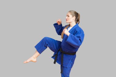 Siyah ayak ile delme ve uzak seyir gri arka plan üzerinde Japon dövüş sanatları kavramı kemer ile Mavi kimono kadında agresif atletik karate yan görünüm 