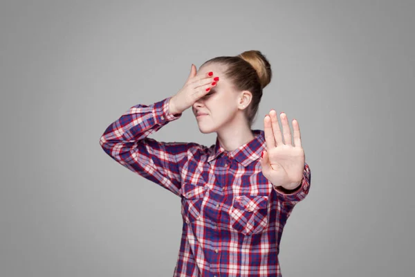 美丽的金发碧眼的女人在粉红色格子衬衫与收集包子发型覆盖眼睛和阻止与手在灰色背景 — 图库照片