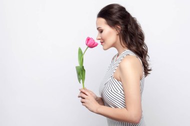 lale tutarak ve gri arka plan kapalı gözler ile kokulu beyaz çizgili elbise makyaj genç esmer güzel kadınla yan görünüm. 