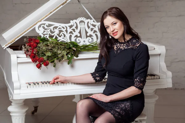 ピアノに座っている赤いバラの花束を持つ美しい女性 — ストック写真