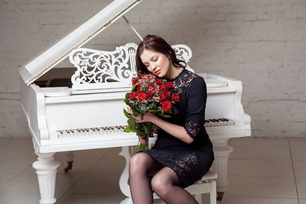 Piękna Kobieta Bukietem Czerwonych Róż Siedząc Przy Fortepianie — Zdjęcie stockowe